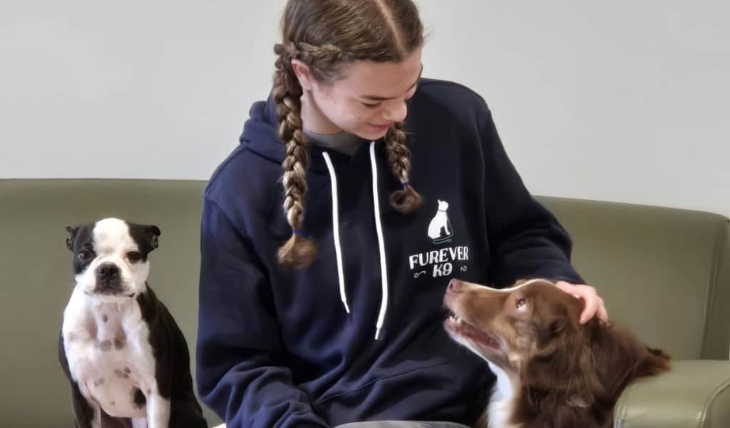 Furever K9 staff member petting a dog while another dog sits beside her on a couch.